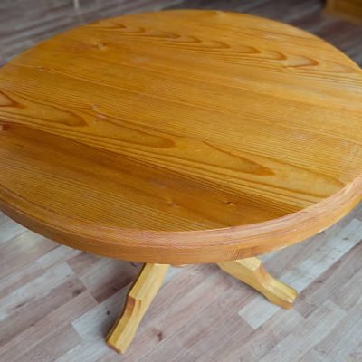 Wooden table on one leg with round table top stand in room with wooden flooring, top view close-up in selective focus